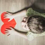 Love in America: A Journey Through Connection and Diversity. .boy in green shirt holding red paper heart cutout on brown table