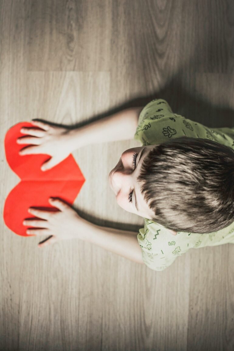 Love in America: A Journey Through Connection and Diversity. .boy in green shirt holding red paper heart cutout on brown table