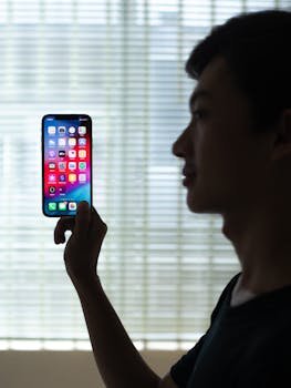 America and Social Media: A Deep Dive into Influence, Impact, and Evolution. 2 America and Social Media: A Deep Dive into Influence, Impact, and Evolution.Profile of a man holding a smartphone with colorful apps, backlit indoors.