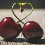 The 10 Amazing Benefits of Love for Health and Happiness (2025)happiness,mental health,benefit of love,Close-up of two ripe cherries with heart-shaped stems on a wooden table, symbolizing love.