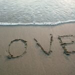Love and Health in 2025: How Emotional Wellness Shapes Physical Vitality.(Love written in sand with ocean waves at the beach, evoking romance and tranquility.)