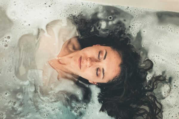 Health in 2025: Socioeconomic and Demographic Factors Influencing Mental Health and Gun Violence in the U.S. and Australia 2 Health in 2025: Socioeconomic and Demographic Factors Influencing Mental Health and Gun Violence in the U.S. and Australia, Woman with long hair enjoying a peaceful bubble bath with eyes closed, illustrating relaxation.